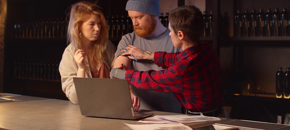 Man wants a tattoo on his arm. Tattooist and woman listen to him