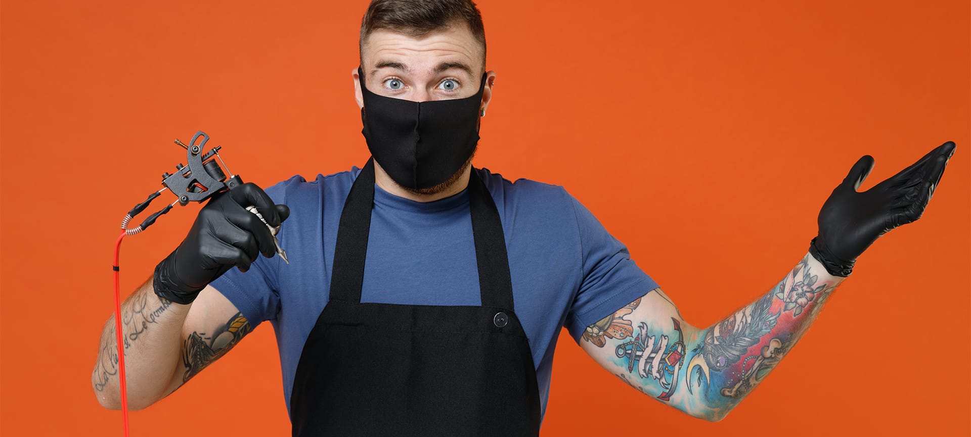 artist tattooed man in t-shirt apron face mask hold machine black ink in jar equipment
