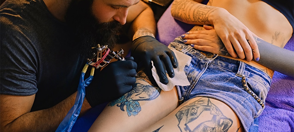 bearded tattoo male artist makes a tattoo on a female leg
