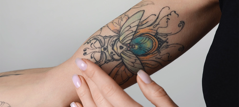 woman applying cream on her arm with tattoos against light background, closeup